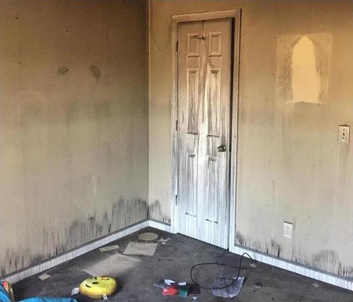 This is a photo of a room that was damaged by a house fire. You can see the soot on the walls, carpet, and door. 